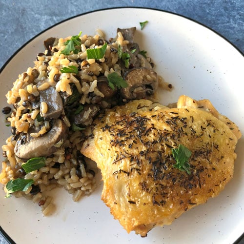 Plate with chicken thigh, brown rice and mushrooms. 