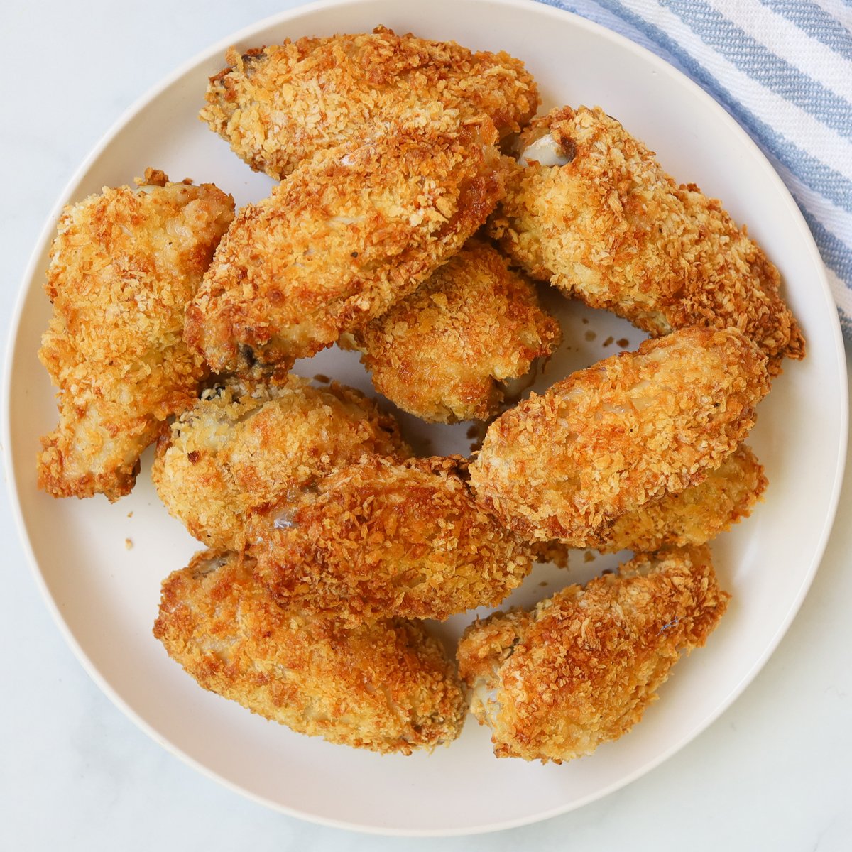 Picture of golden, crispy breaded chicken wings on a white plate. 