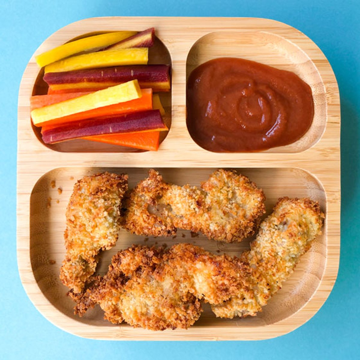 Toddler plate with chicken strips, ketchup and carrot sticks.