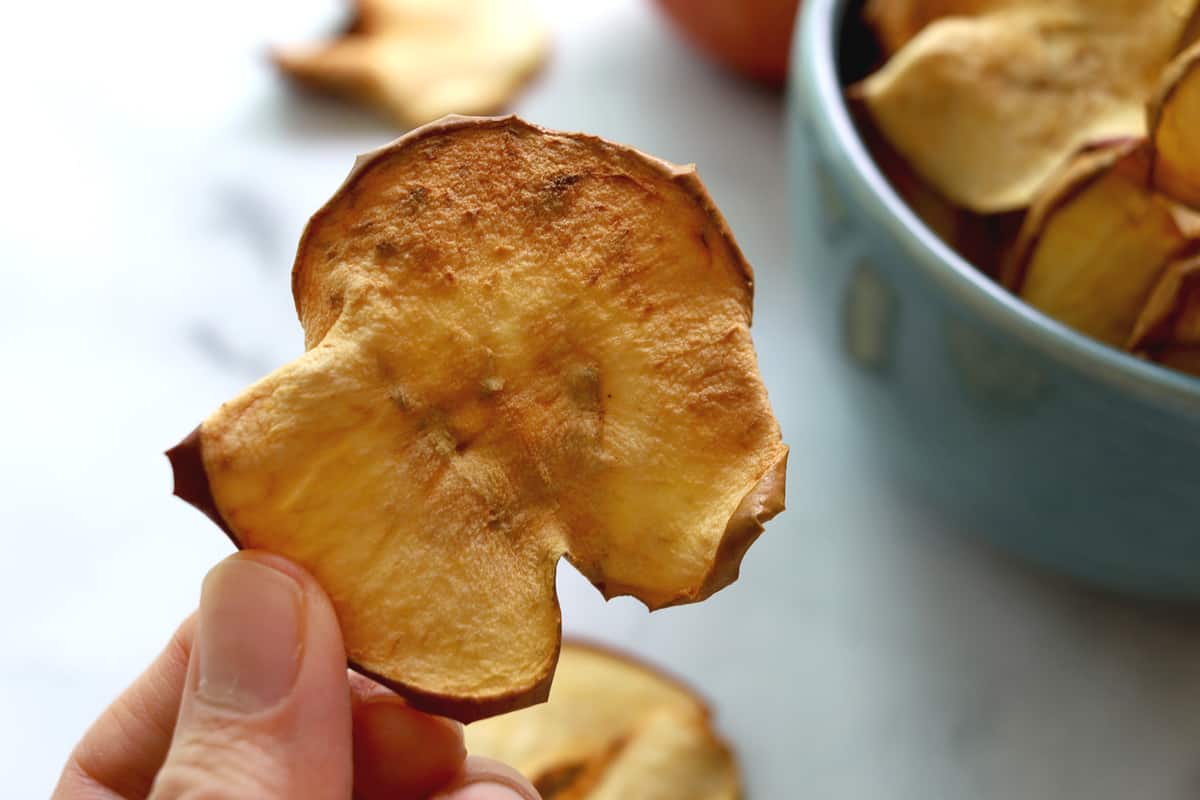 Close up of apple chip. Apple chips in a bowl in background. 