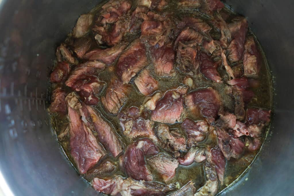 sliced undercooked meat submerged in stock in a pot.