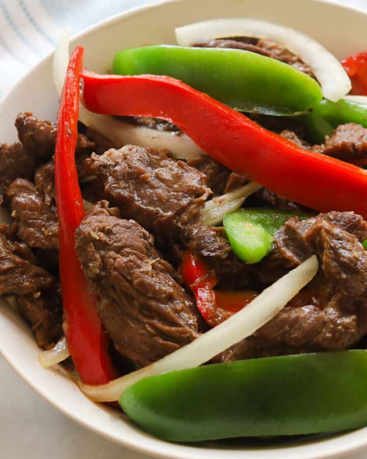 Plate with beef, sliced red and green bell peppers and white onions.