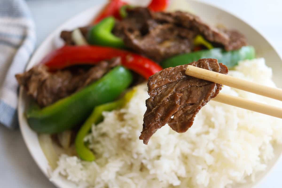 Plate with beef, sliced red and green bell peppers and white onions. Closeup of chopsticks and beef.