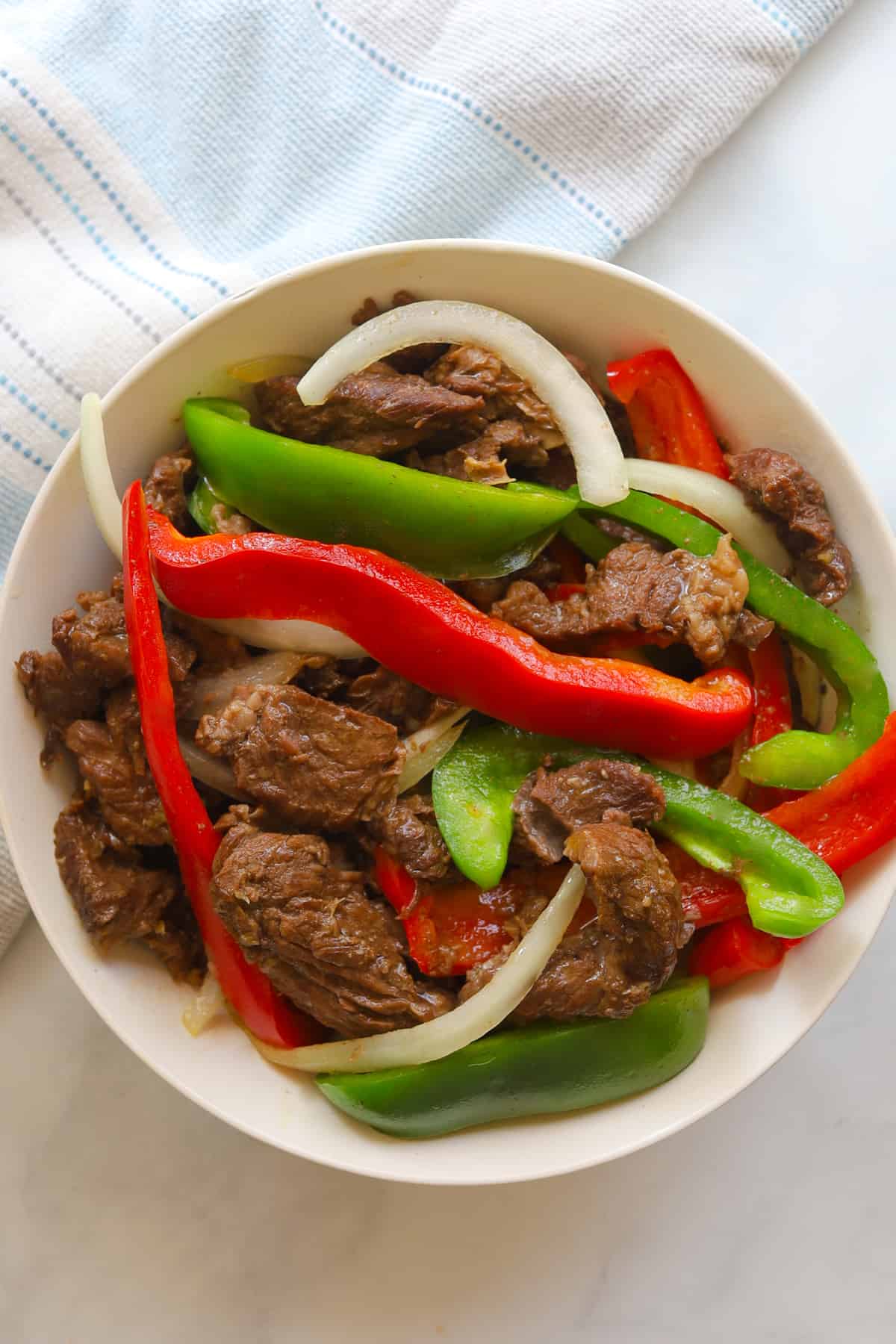 Plate with beef, sliced red and green bell peppers and white onions.