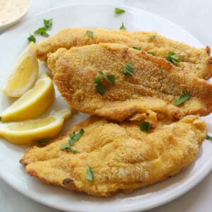 3 golden crusted fish fillets garnished with lemon wedges and parsley leaves.