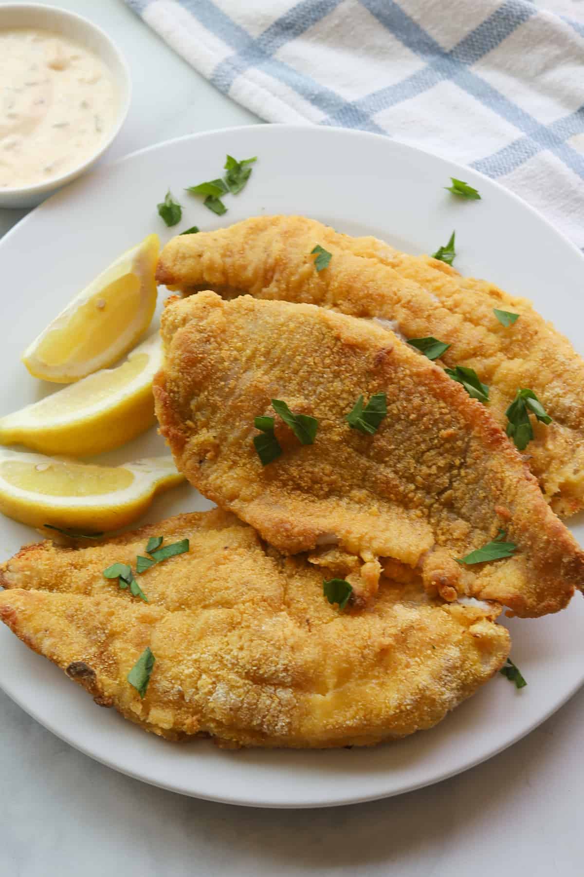 3 golden crusted fish fillets on a plate, garnished with lemon wedges and parsley leaves