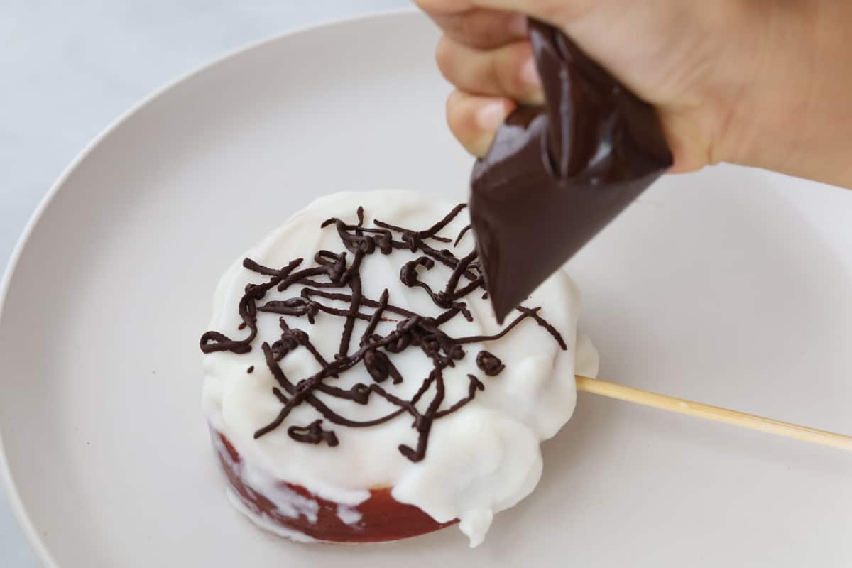 hand decorating yogurt covered apple with chocolate sacue