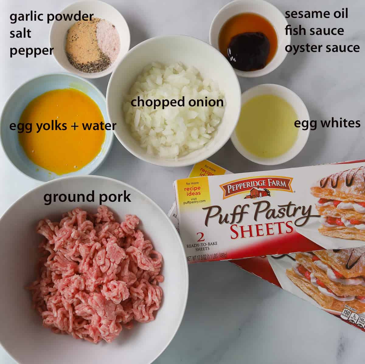Layout of ingredients in a bowl. Ground pork, egg wash, seasoning, chopped onions, egg whites, sauces. 2 puff pasty boses.