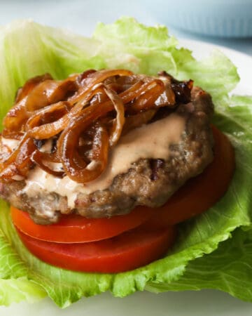 burger patty with sliced tomatoes, caramelized onions and sauce on a bed of lettuce.