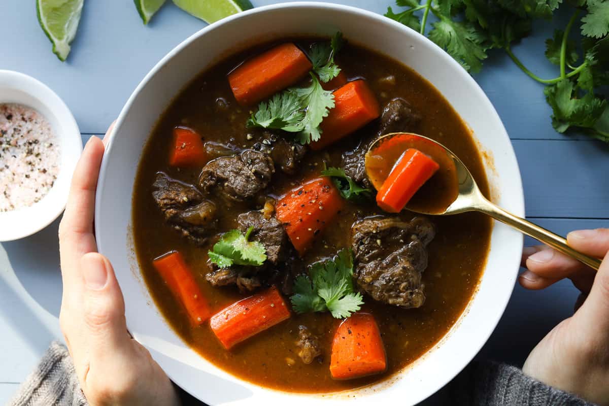 Closeup of a bowl with beef and carrot stew. Garnished with cilantro leaves.