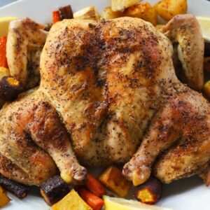 Roasted whole chicken with colored carrots and potatoes on a plate.