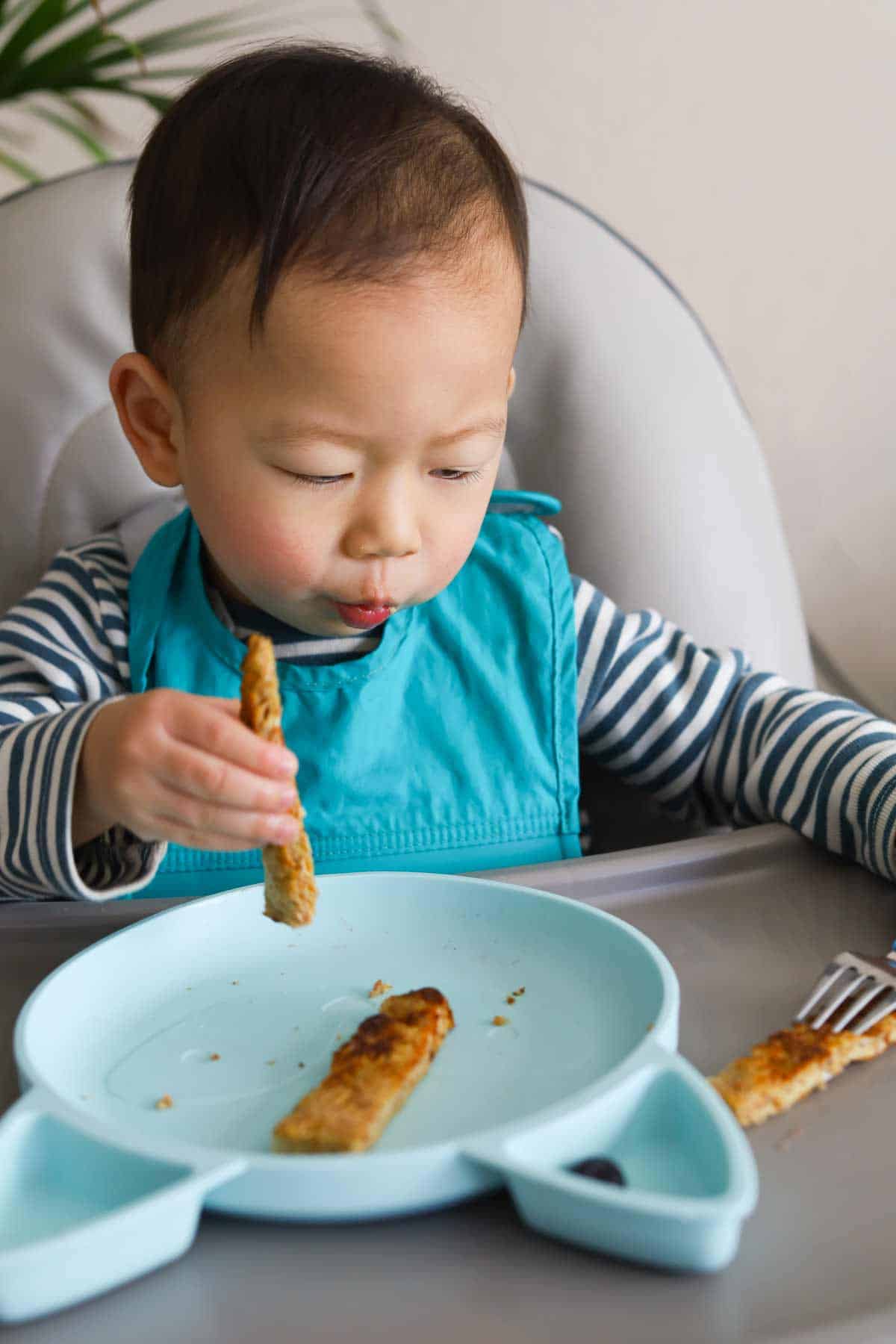Baby eating sliced piece of bread with fork in hand.