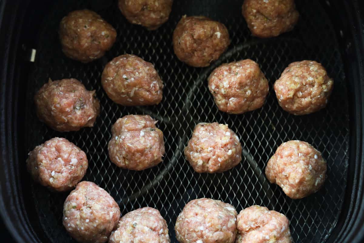 Uncooked meatballs in an air fryer basket.