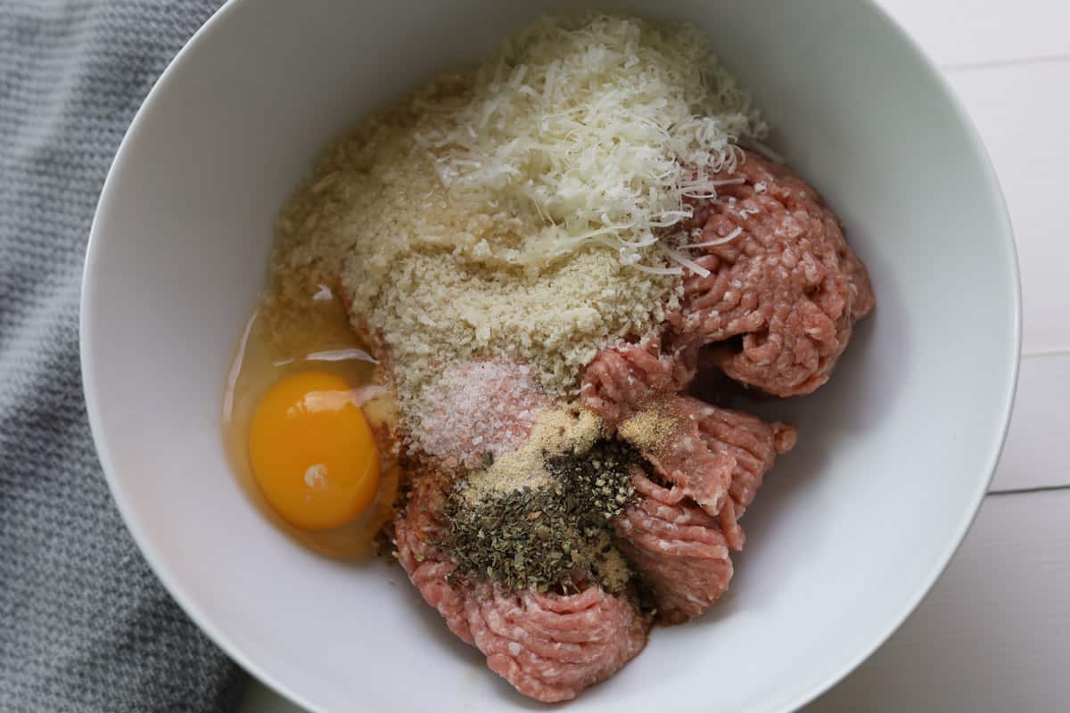 Image of ingredients in a bowl; grated cheese, ground turkey meat, panko crumbs, an egg and seasoning in a bowl.