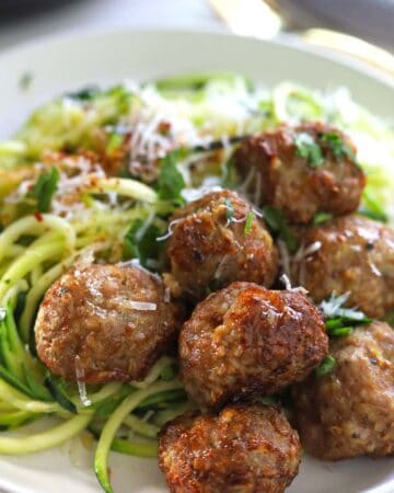 Golden brown meatballs with zucchini noodles garnished with grated cheese and chopped parsley.