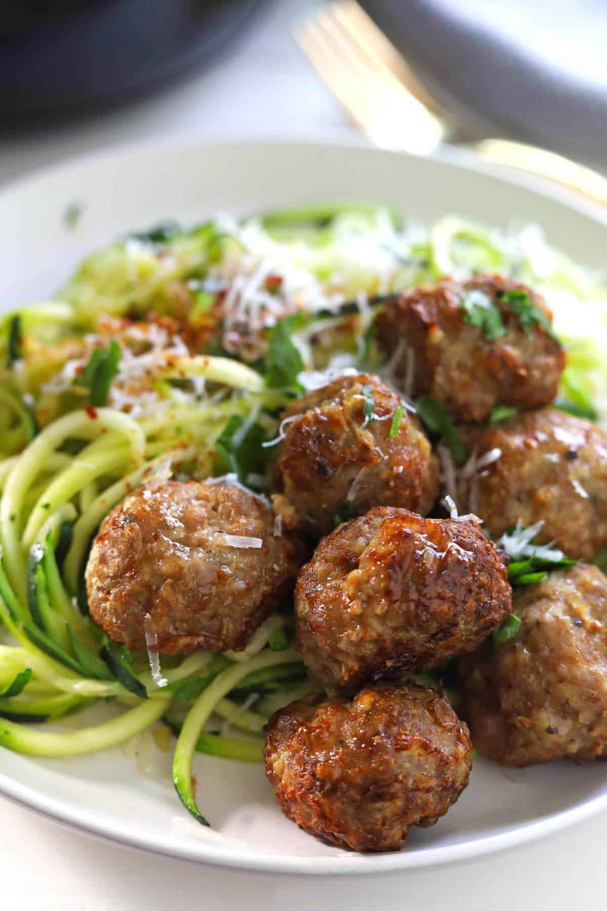 Golden brown meatballs with zucchini noodles garnished with grated cheese and chopped parsley.