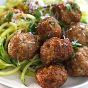 Golden brown meatballs with zucchini noodles garnished with grated cheese and chopped parsley.