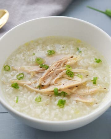 A bowl of rice porridge with shredded chicken, garnished with green onions.