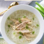 A bowl of rice porridge with shredded chicken, garnished with green onions.