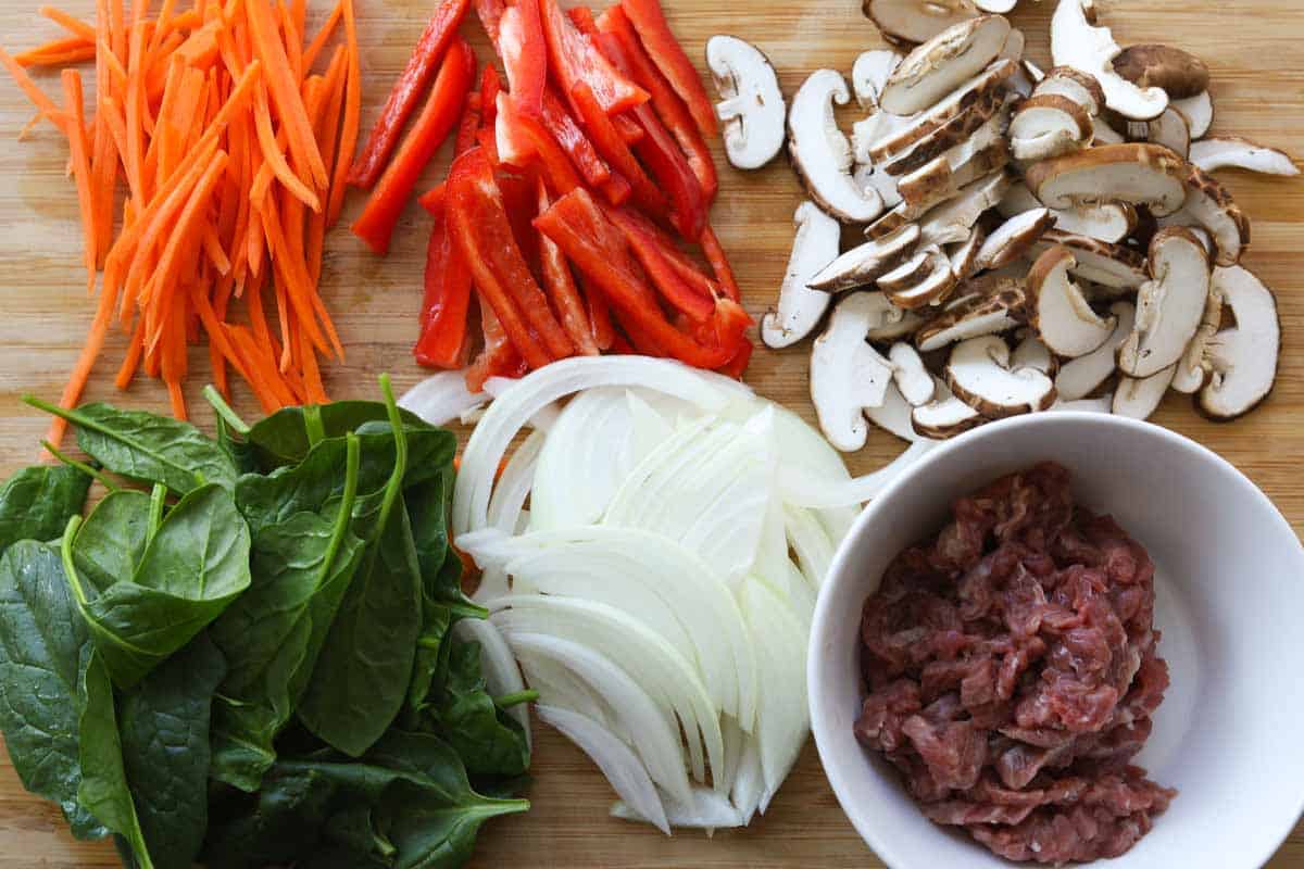 Image of cutting board with sliced carrots, bell peppers, mushrooms, onions and beef. 
