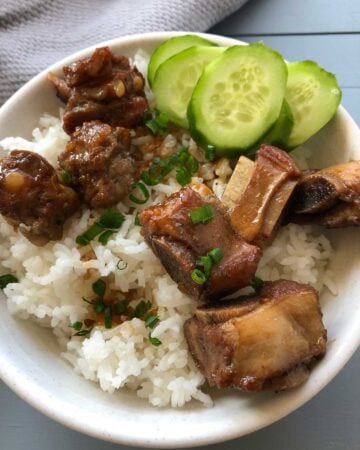 Bowl of rice with pork riblets, sliced cucumbers, garnished with green onions.