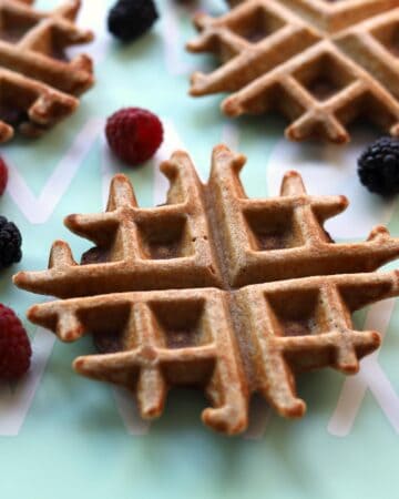Closeup of waffle and scattered raspberries and blackberries.