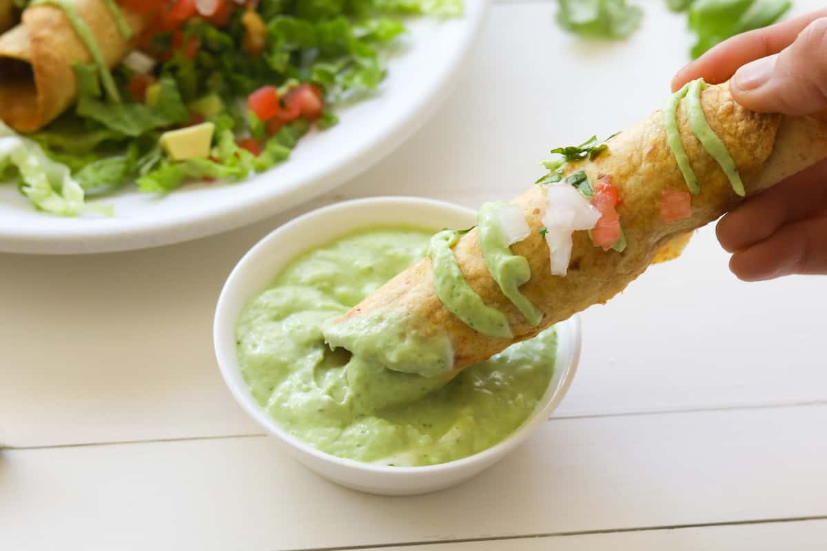 taquito being dipped in a avocado crema sauce.