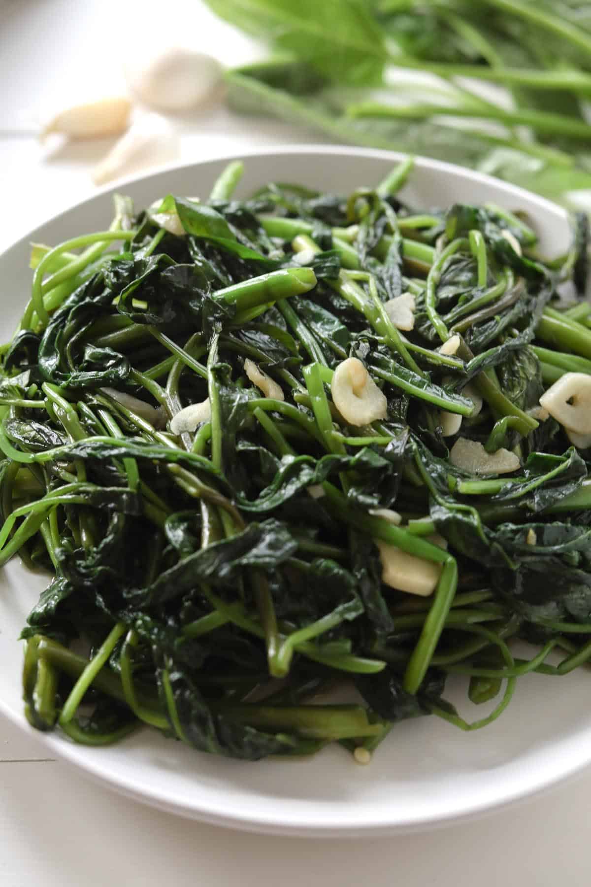 Plate of cooked morning glory with slices of cooked garlic. 