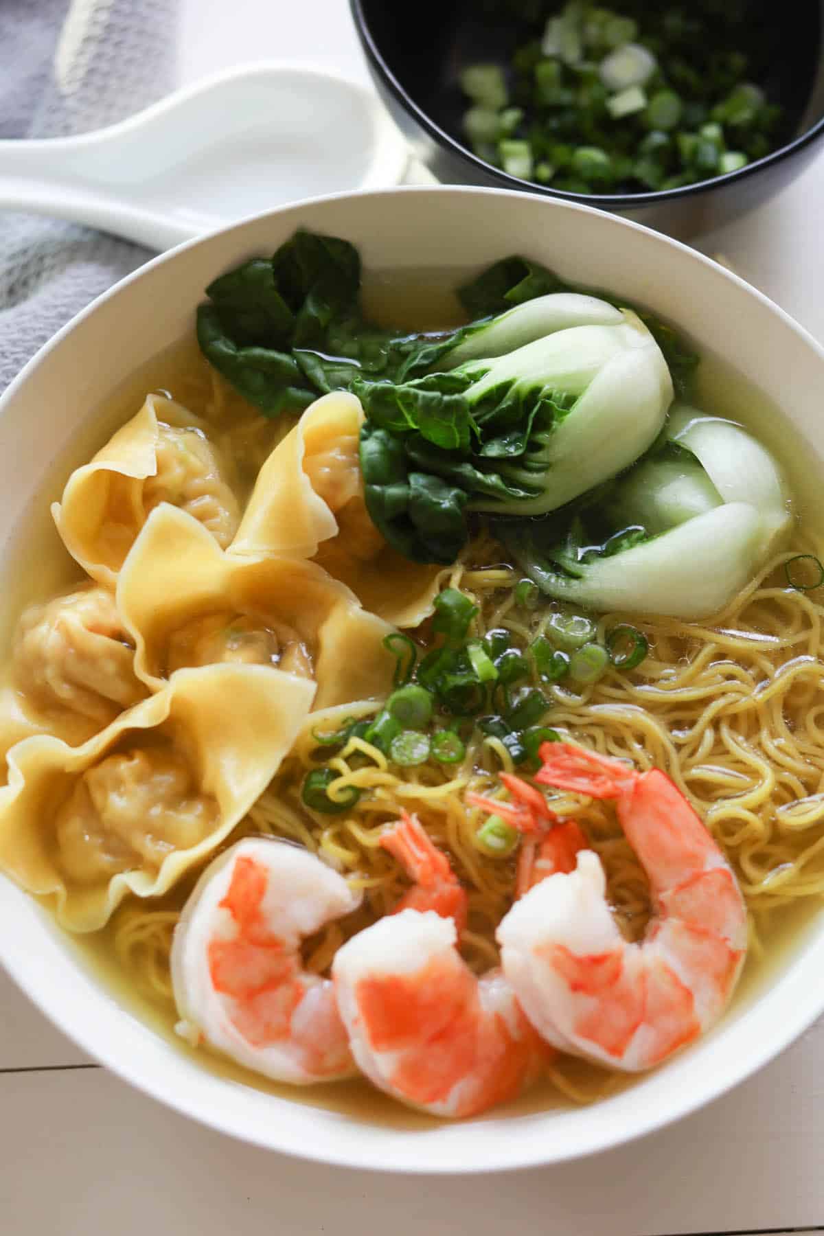 Bowl of egg noodles in broth with shrimp, bok choy and wontons, garnished with green onions.