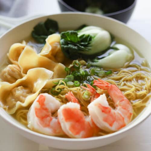 Bowl of egg noodles in broth with shrimp, bok choy and wontons, garnished with green onions.