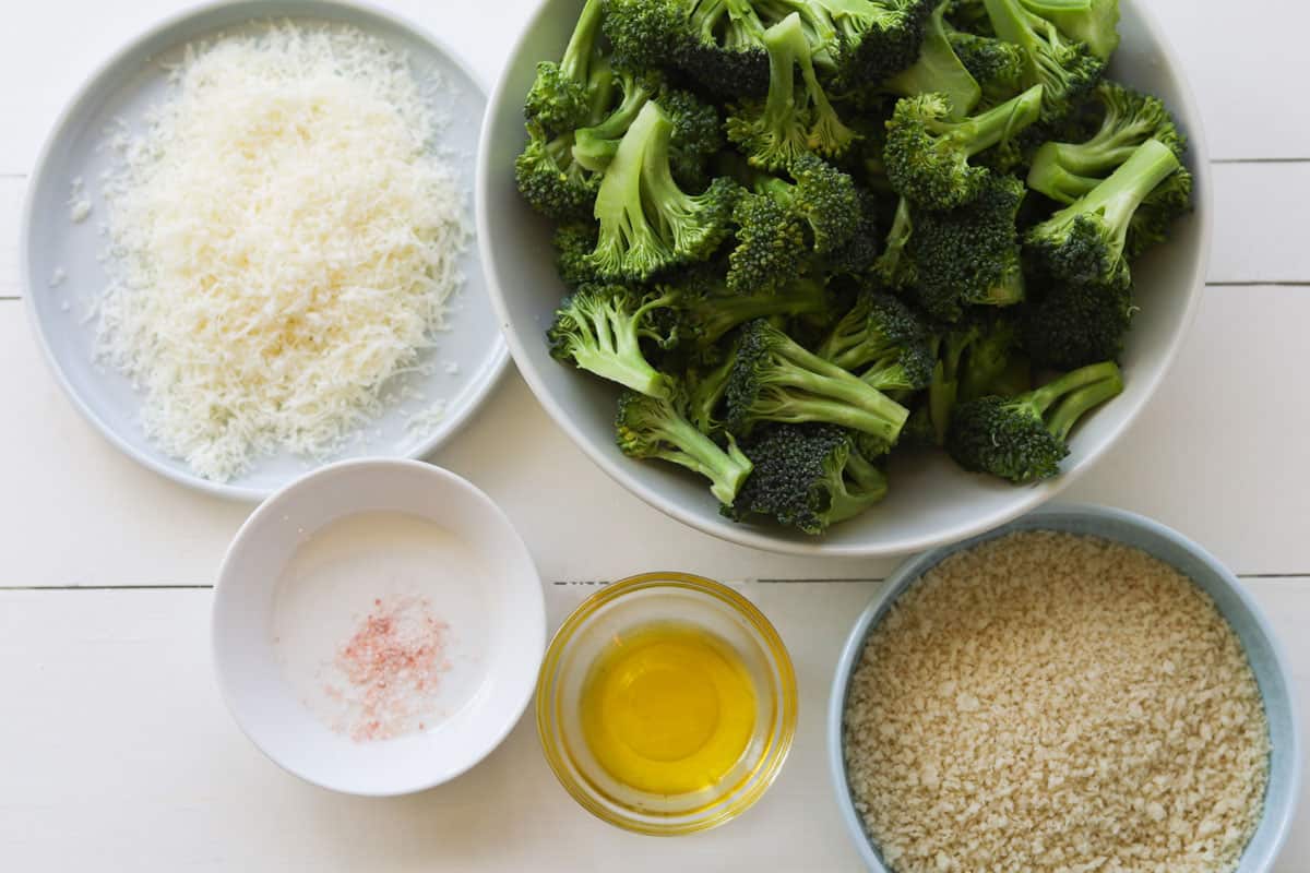 Image of ingredients, grated parmesan, broccoli florets, salt, oil in a bowl and panko crumbs.