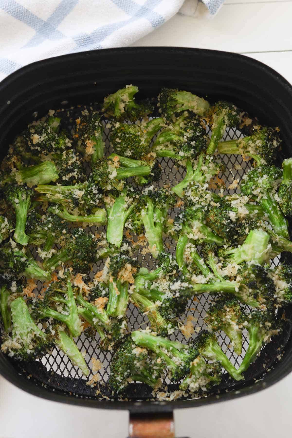 Roasted broccoli florets crusted with parmesan and panko in an air fryer basket.
