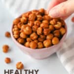 Close up image of finger picking up roasted chickpeas with seasoning from a bowl.