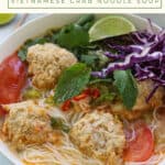 Bowl of rice noodles with soup, crab meatballs, tomatoes and garnished with fresh greens and herbs.