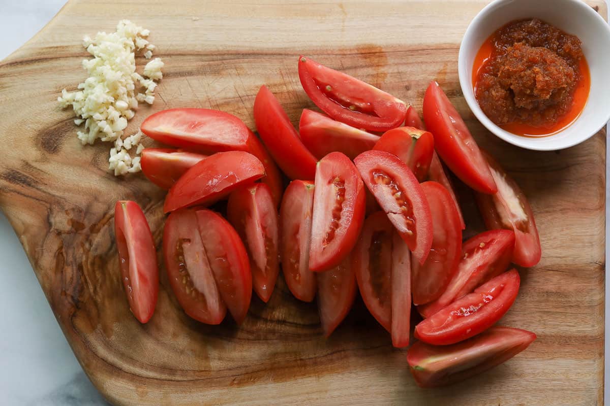 Tomato wedges, minced garlic and crab paste on a cutting board.