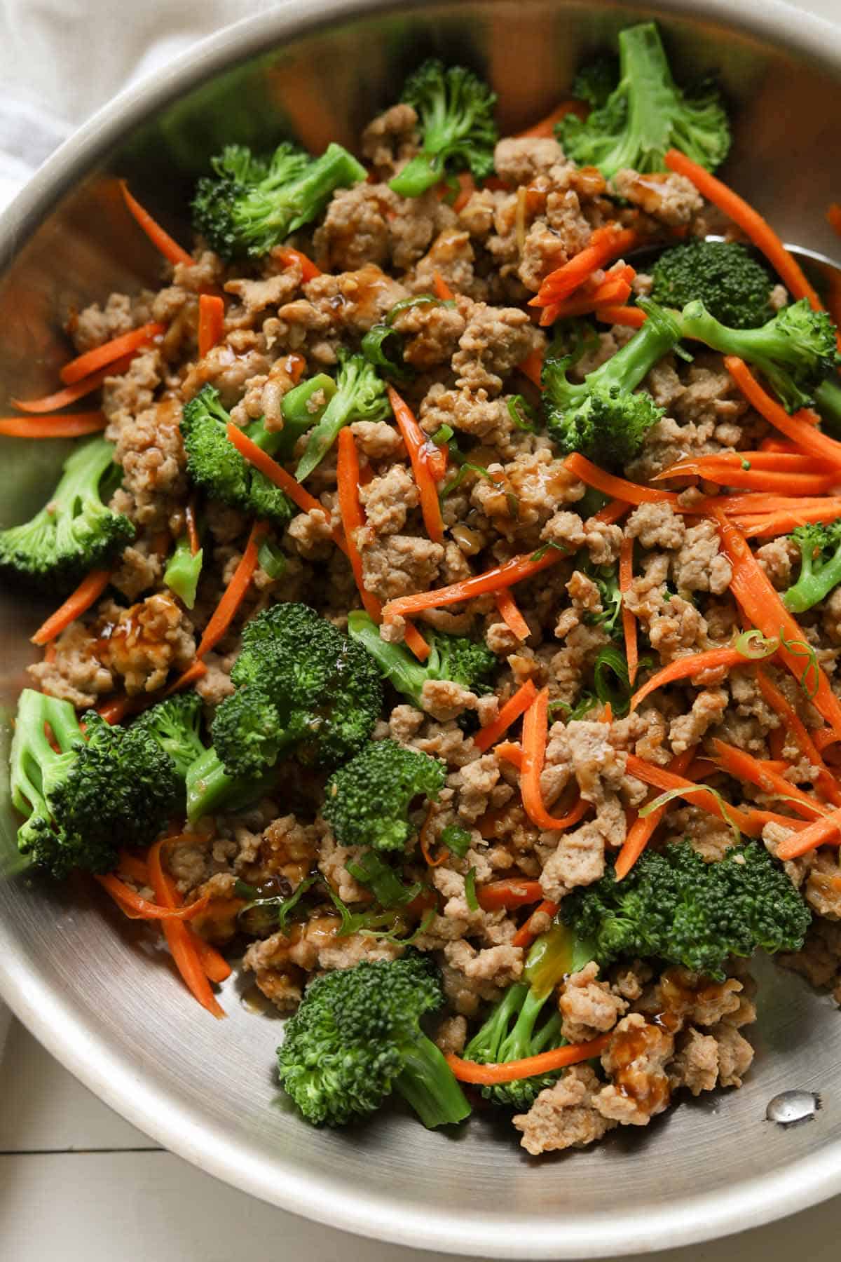 Close up of ground meat stir fry with broccoli florets and julienned carrots in a pan.