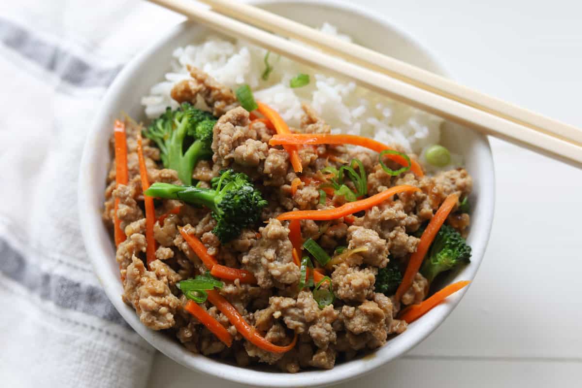 Bowl of rice with ground meat with broccoli florets and julienned carrots stirfry.