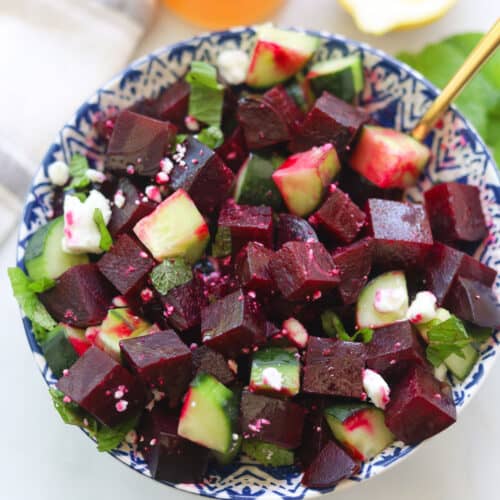 Red beet and cucumber salad bowl topped with feta and mint leaves.