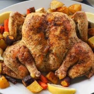 Whole roasted chicken with vegetables on a plate.