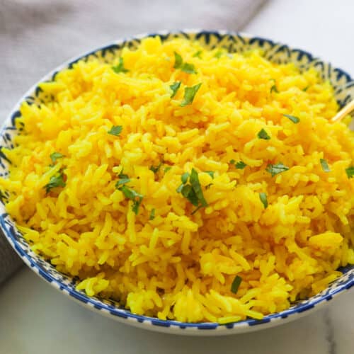 Bowl of yellow rice with cilantro leaves.