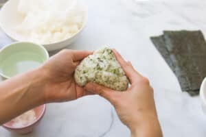 Molding rice ball into a triangle with hands.