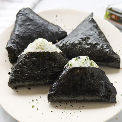 Four triangle shaped rice balls wrapped in seaweed on a plate.