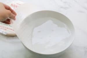 Rice paper being dipped in bowl of water.