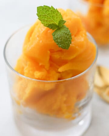 Mango sorbet garnished with mint leaves in a cup.