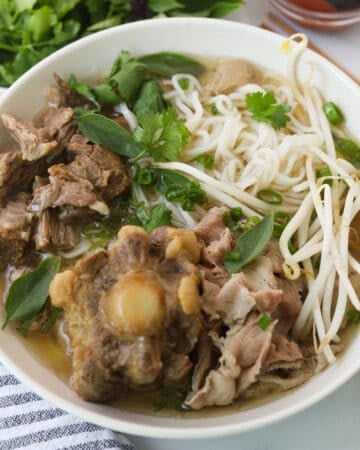 Bowl of rice noodle soup with beef and herbs.