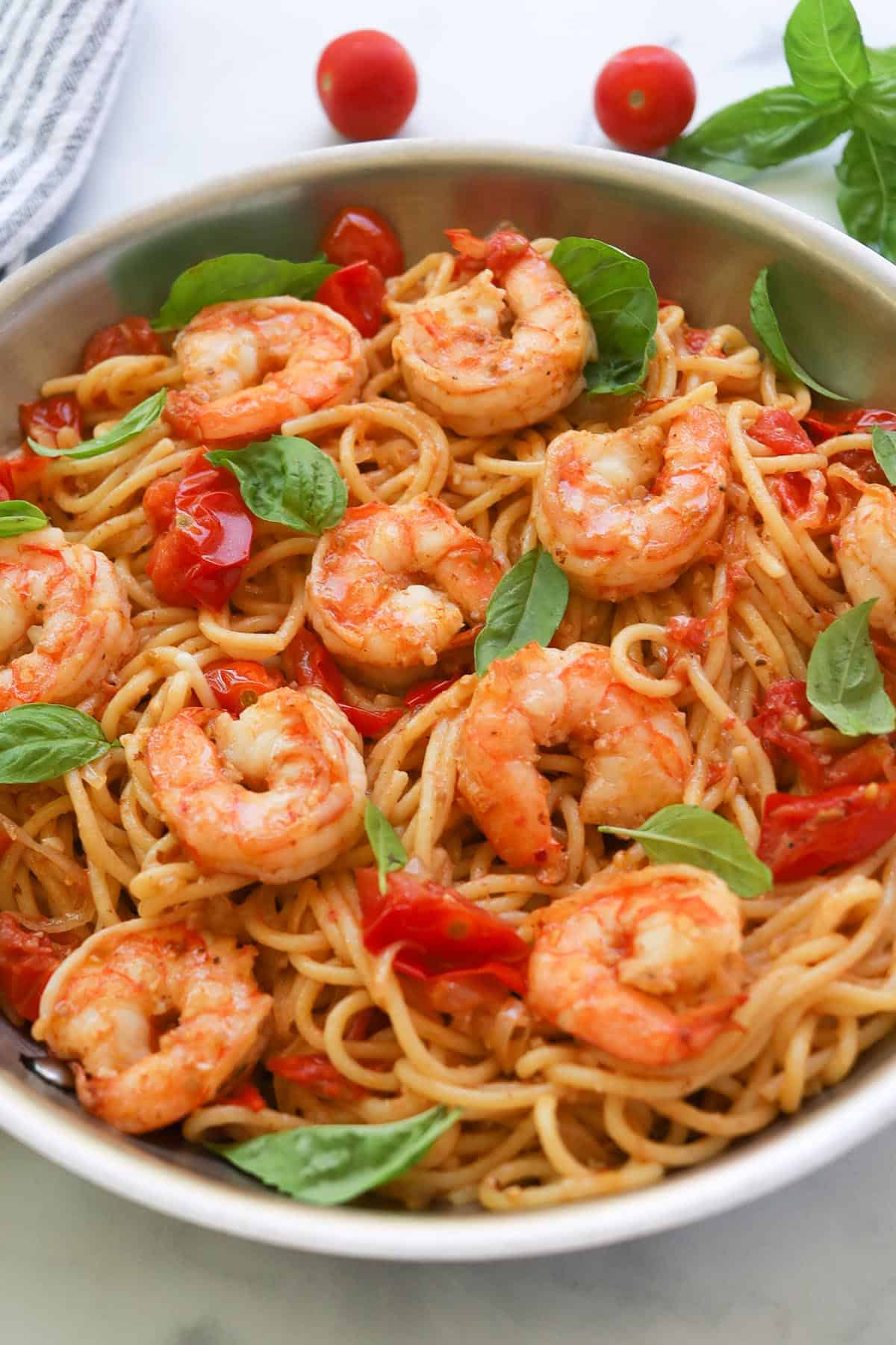 Shrimp pasta with cherry tomatoes and basil on plate.