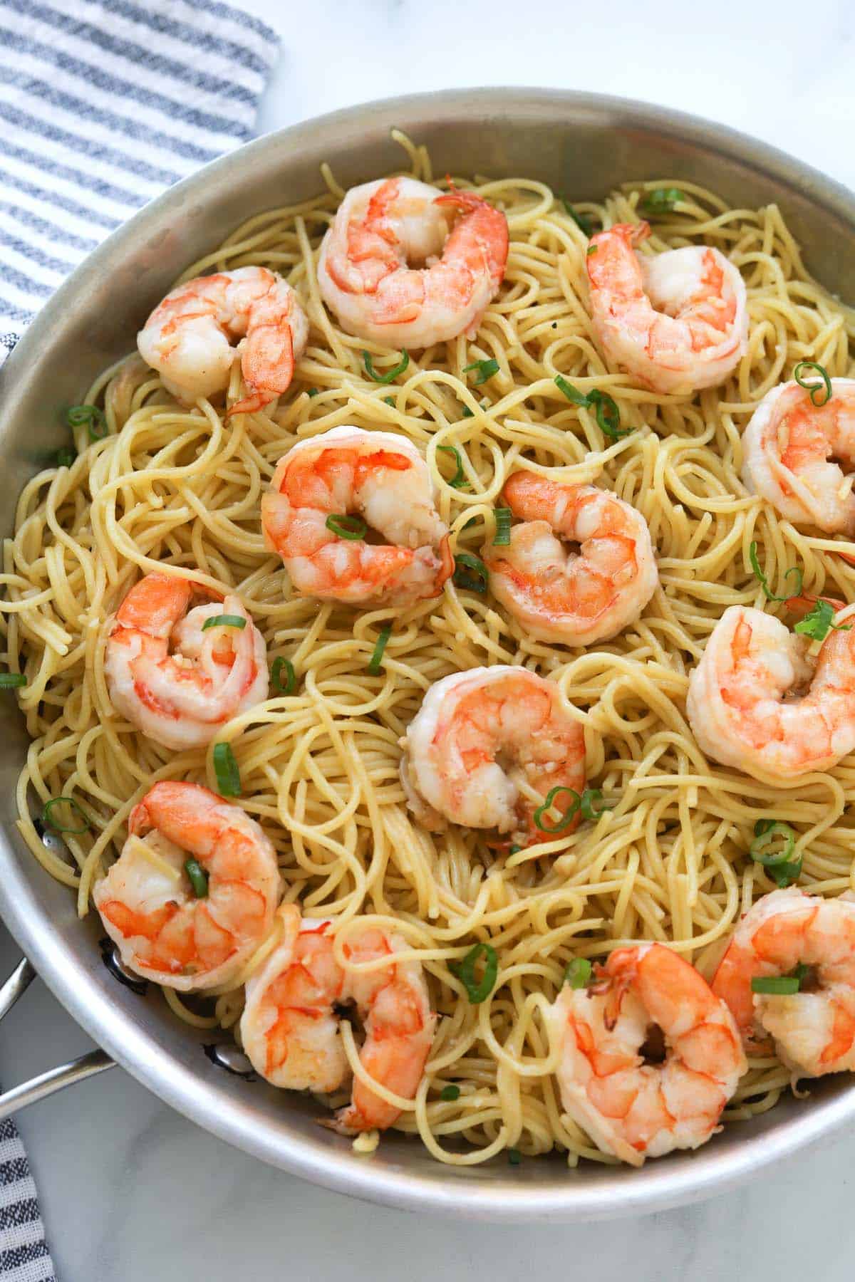 Noodles with shrimp and green onion garnish in pan.