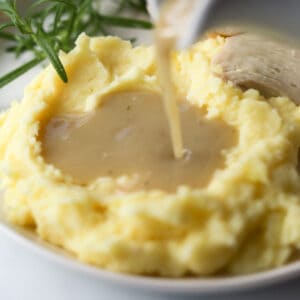 Gravy being poured onto mashed potatoes.