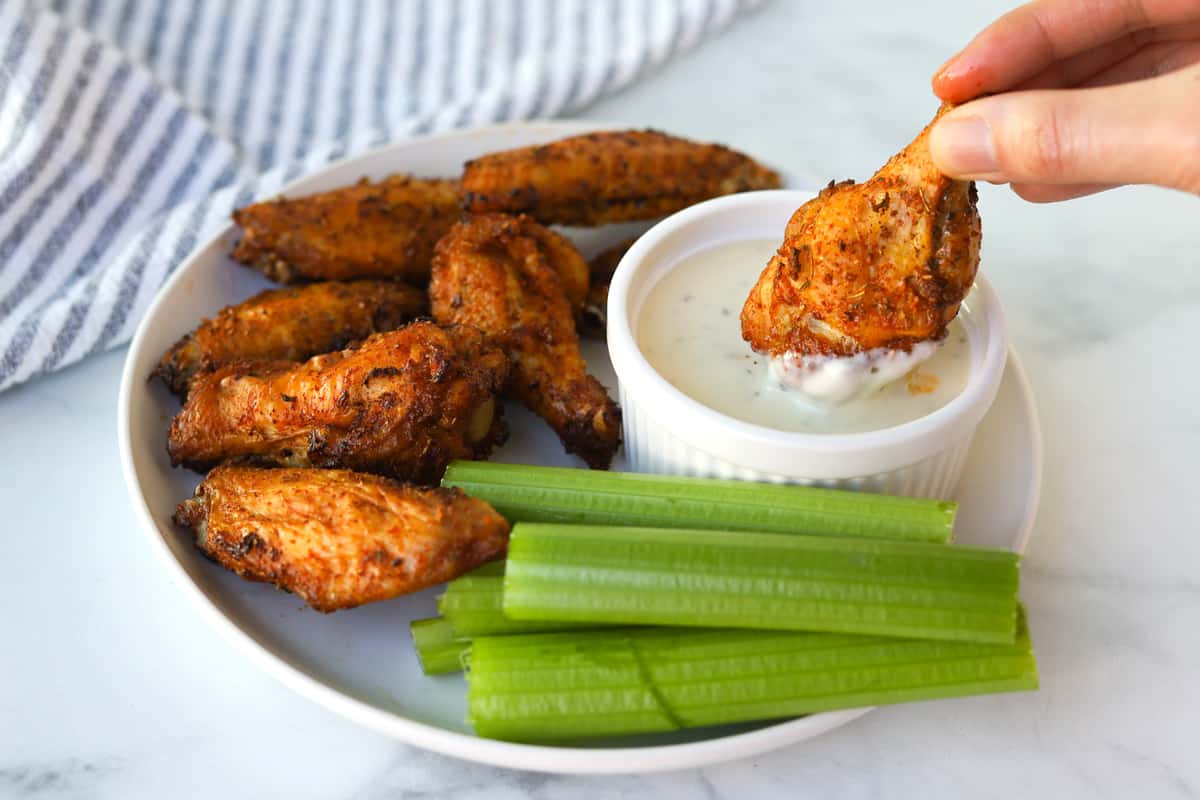 Hand dipping chicken wings in sauce.
