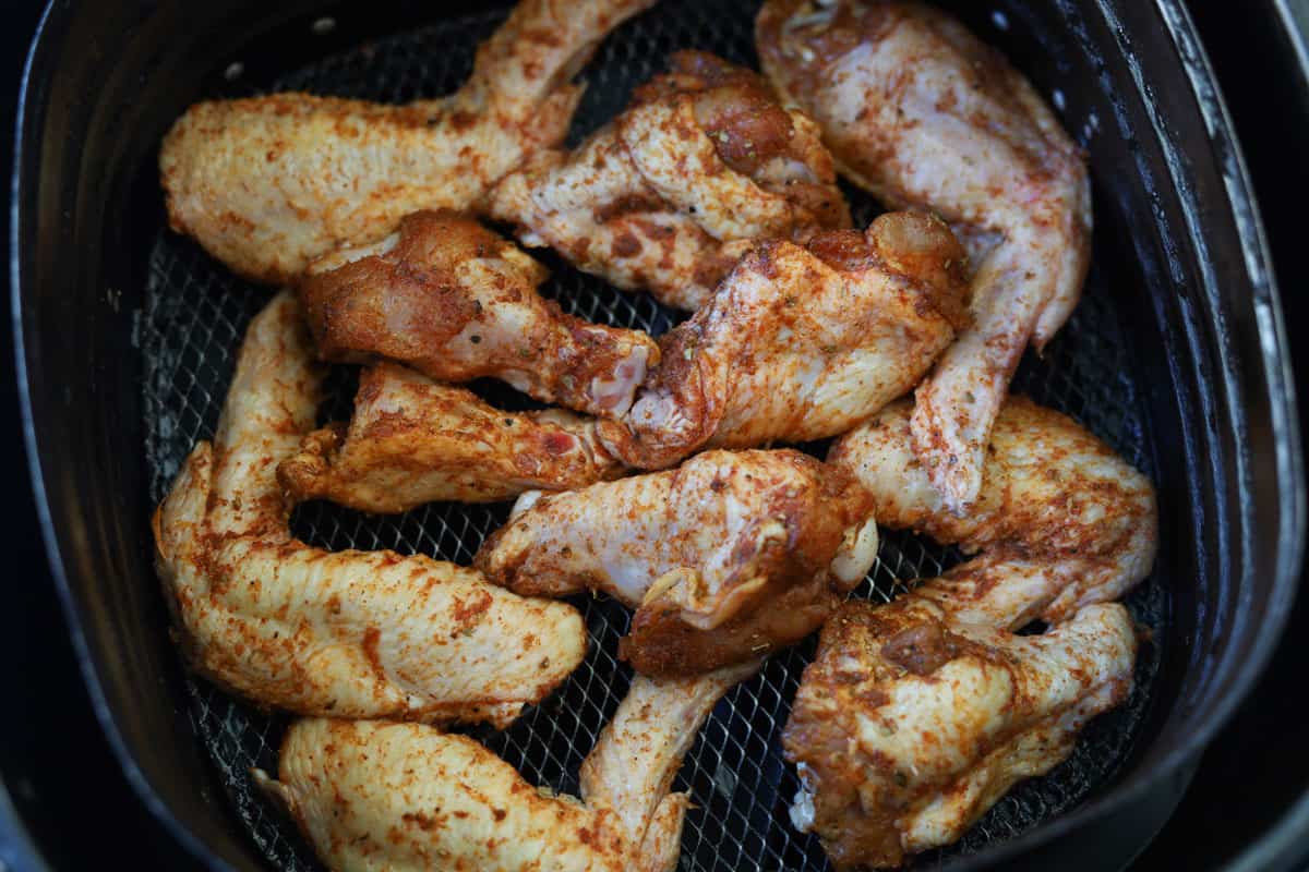 Uncooked chicken wings with seasoning in air fryer basket.